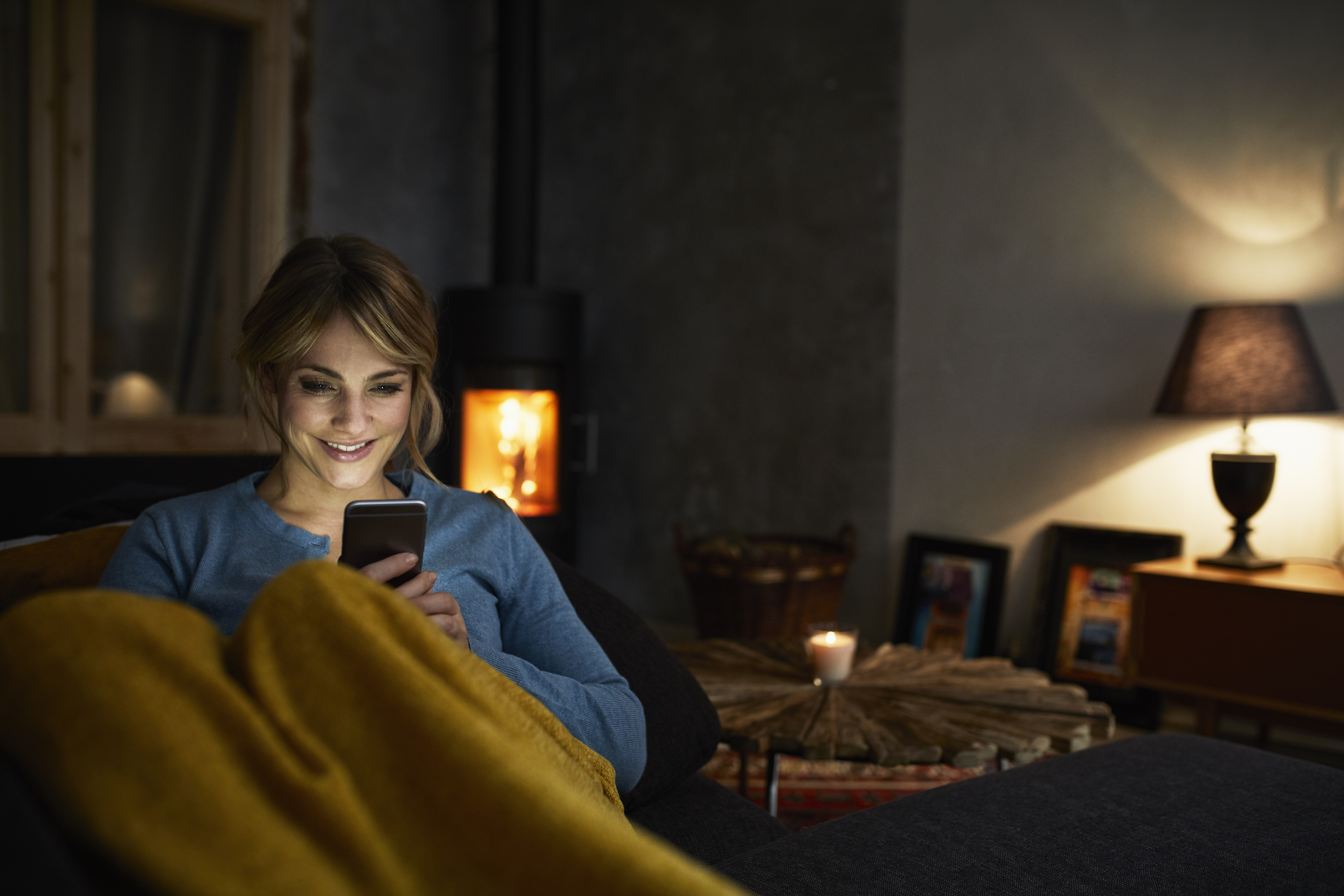 Woman at home on couch with blanket in dim lighting