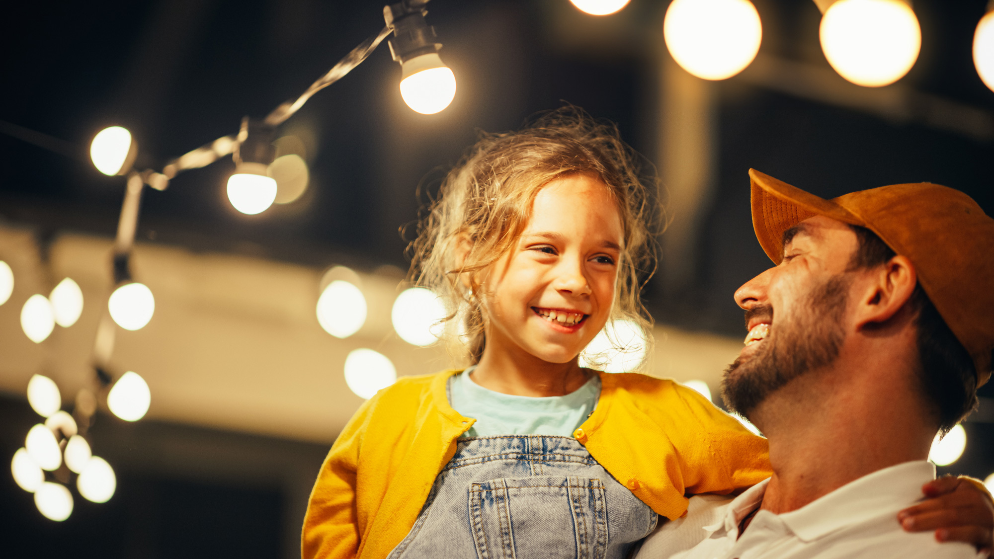 Father and daughter laugh together under fairy lights