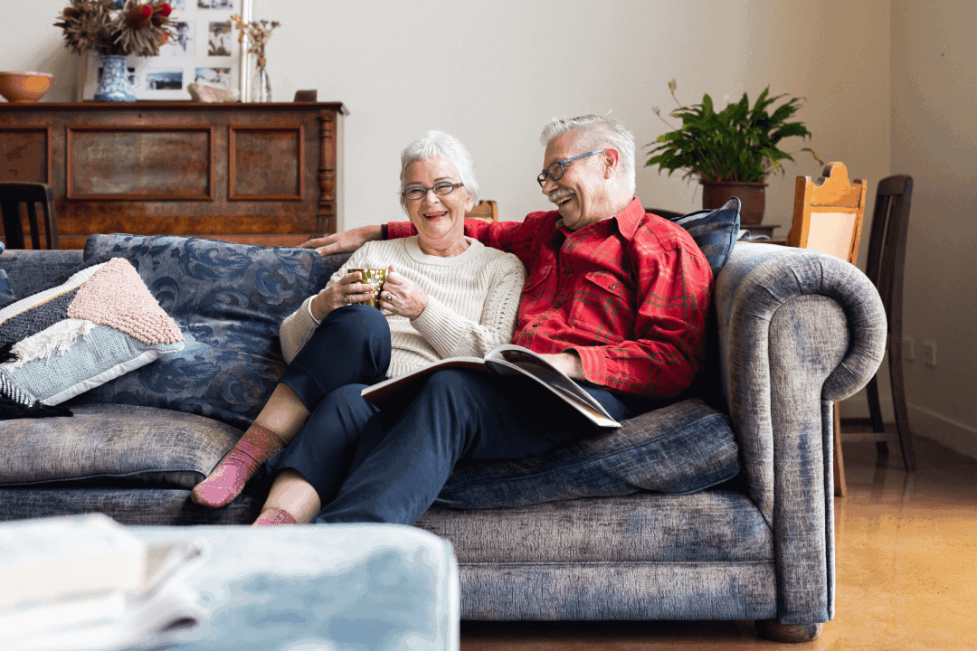 Old couple laughing at home on the couch 1