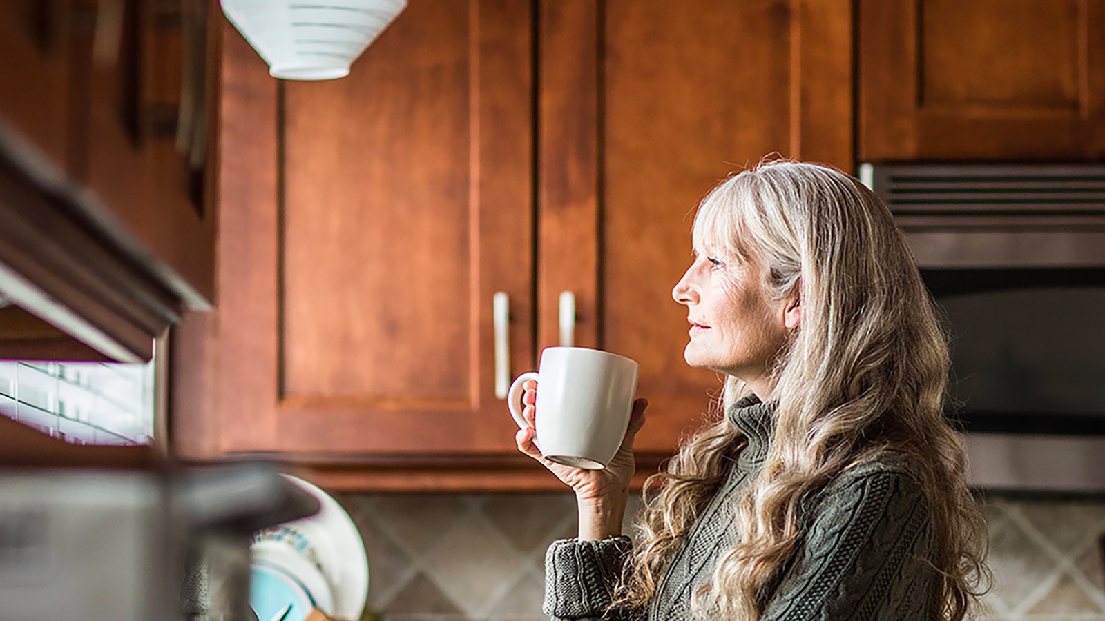 Woman standing in her kitchen drinking tea