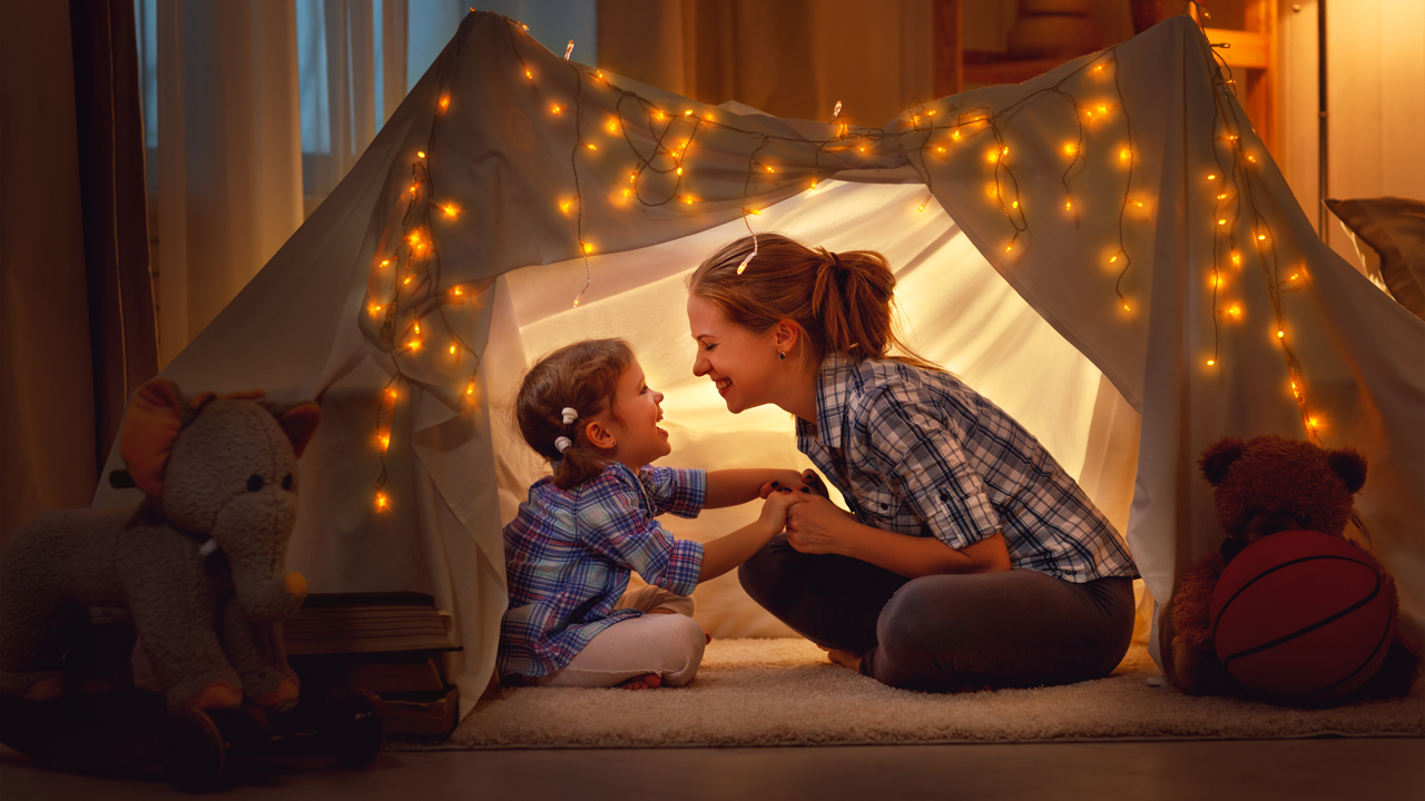 Woman and child laughing inside an indoor tent with fairy lights